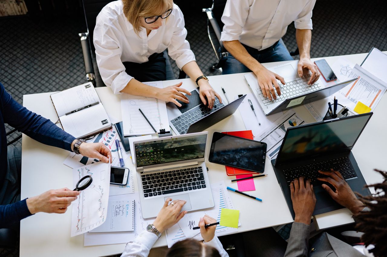 about-us Overhead view of a corporate team collaborating with laptops and documents.